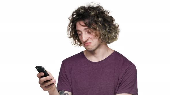 Portrait of Modern Guy with Curly Hair in Casual Tshirt Browsing Internet on Smartphone and Finding