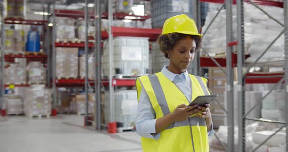 Female Factory Manager Using Digital Tablet in Warehouse While Standing Against Goods Shelf