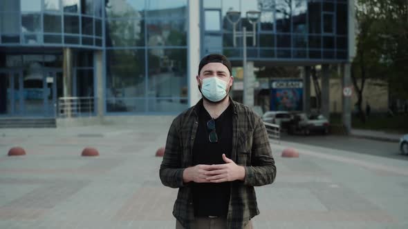 Man in Medical Mask Talking Confidently Into Camera with Gestures on City Area