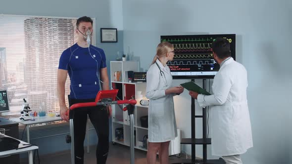 Multiracial Scientists Examining the Athlete's Medical Records While He Stress Testing in Lab