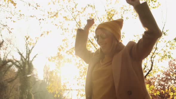 Positive Woman Dances in Sunny Autumn Forest on Warm Day