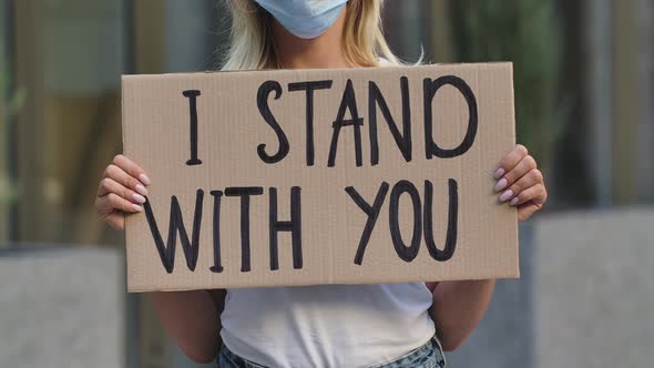 I STAND WITH YOU on a Cardboard Poster in the Hands of Female Protester Activist in a Medical Mask