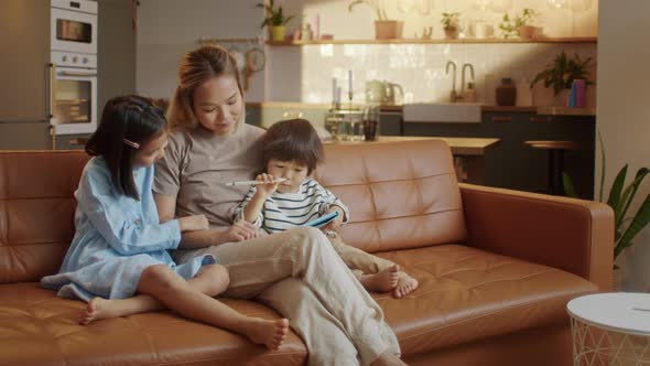 Happy Asian Family Using Tablet Computer With Children Mother Watching Kids Play Game on Touchscreen