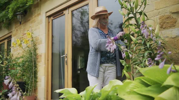 A woman gardening outside her home wearing a face mask on