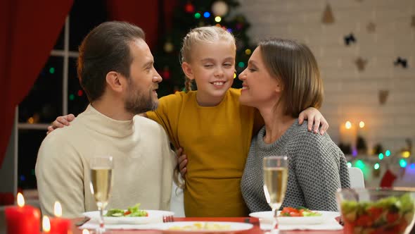 Parents Kissing Happy Child, Looking at Camera, Christmas Tree Twinkling Behind