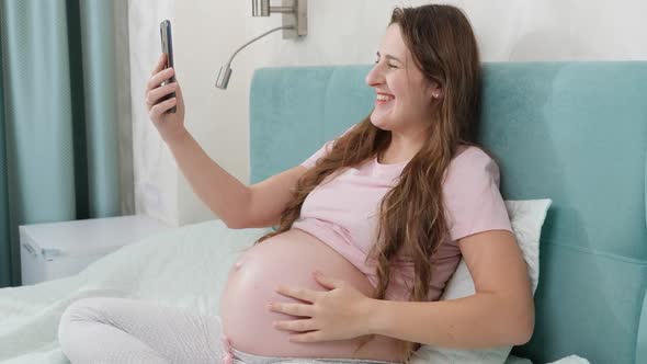 Portrait of Happy Smiling Pregnant Woman Having Video Talk or Conference on Smartphone