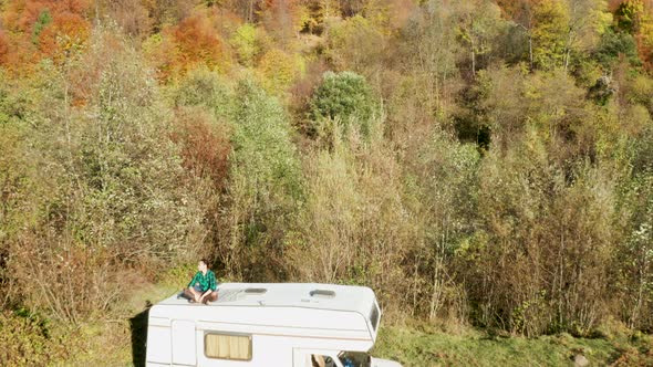 Drone Flying Over Girl on Top of Retro Camper Van in the Fores