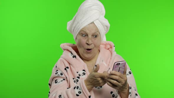 Elderly Grandmother in Bathrobe. Old Woman Using Social Media App on Smartphone