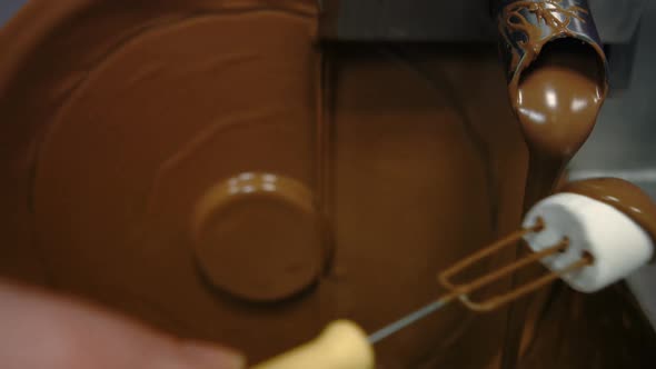 Worker dipping marshmallow with fork in chocolate blending machine