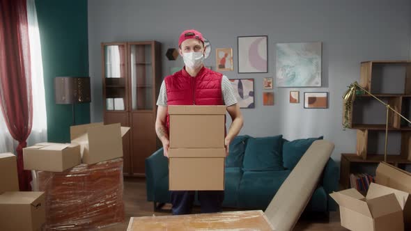 Delivery Man with Covid Mask Holding Carton in New Apartment and Looking at Camera