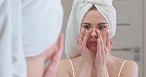 Young Female Stands in Front of the Mirror in Her Bathroom and Applies Cream on Her Face, Skin Care