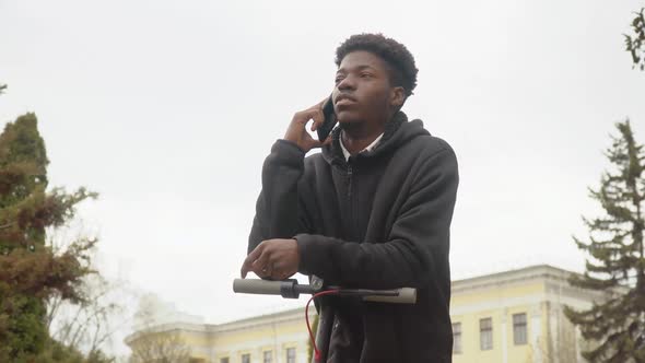 A Young AfricanAmerican Man in a Black Sweater and Black Jeans and Sneakers Leans on an Electric