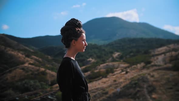 Young Woman with Dreadlocks Standing on a Mountain and Looking Around Then Walks Forwards