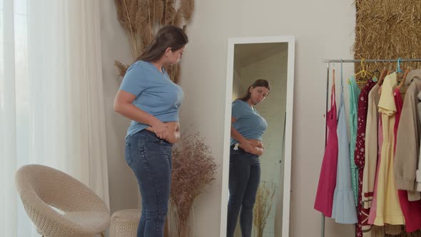 Young Woman Checking Fat on Abdomen Standing in Front Mirror Indoors
