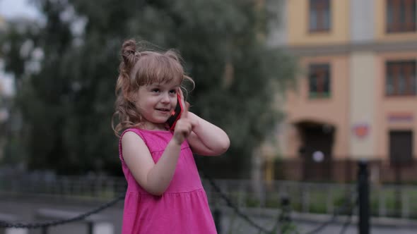 Child Girl Talking By Smartphone Outdoors. Kid in Pink Dress Talking By Mobile Phone on City Street