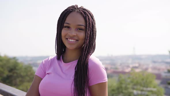 A Young Black Woman Looks Around, Then at the Camera and Smiles - a Cityscape in the Background