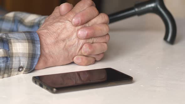 An adult man in stress is waiting with a call. A pensioner's hands and a smartphone close up on the 