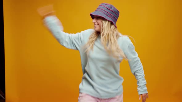 Young Happy Woman in Panama Hat Dancing on Yellow Background