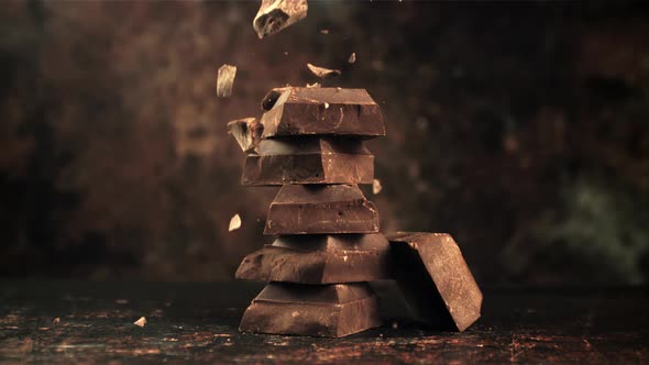 Super Slow Motion Falling Pieces of Bitter Dark Chocolate on a Pyramid of Chocolate Slices