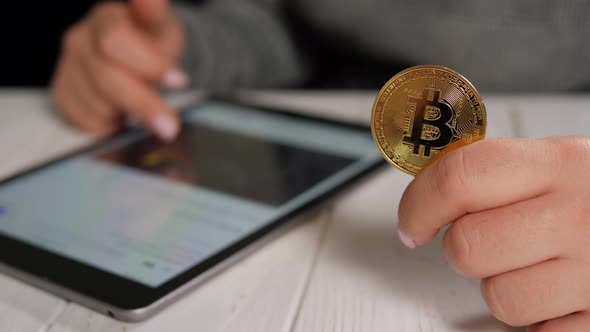 Closeup of a Woman Holding a Silver Bitcoin and Working with Charts on a Tablet