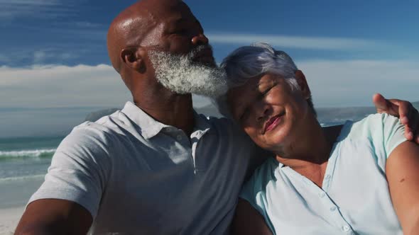 Happy senior african american couple sitting and embracing at the beach