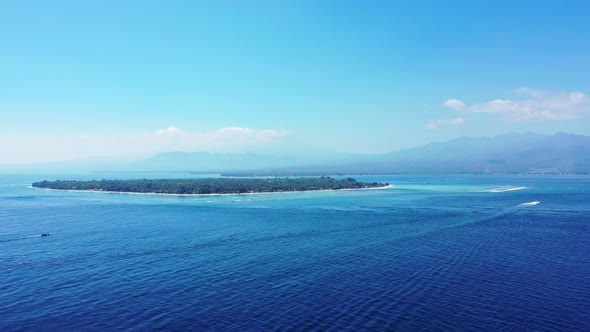 Low-lying tropical island with lush vegetation in Bali surrounded by blue azure sea where boats trac