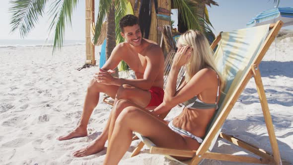 Caucasian couple sitting on sunbeds on the beach