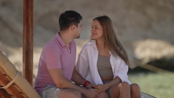 a Woman in a White Shirt with Long Hair and a Man in a Pink Tshirt are Sitting Against the