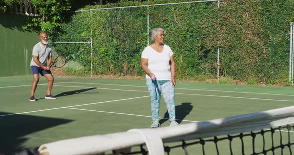 African american senior couple playing tennis on the tennis court on a bright sunny day