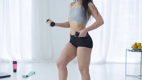 Camera Moves Up Along Slim Fit Body of Young Confident Sportive Woman Lifting Dumbbell and Posing