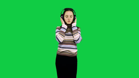 Happy gir with headphones dances in front of the green screen