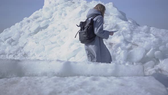 Young Sad Blond Pretty Woman in Warm Jacket Slipping While Walking on the Glacier with Map in Hands