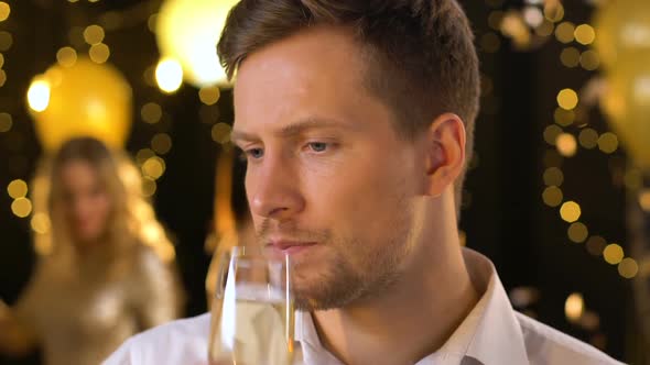 Jealous Unhappy Male Drinking Champagne at Party Alone, While Others Having Fun