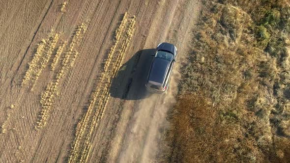 Aerial Top Down View of SUV Car Driving Country Dusty Road Crossing Harvested Field