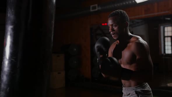 Black Athletic Shirtless Young Man Boxer Training Punching on the Punching Bag with an Effort in the