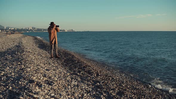 City Dweller Is Walking Over Gravel Shore of Sea and Taking Photos in Sunny Day