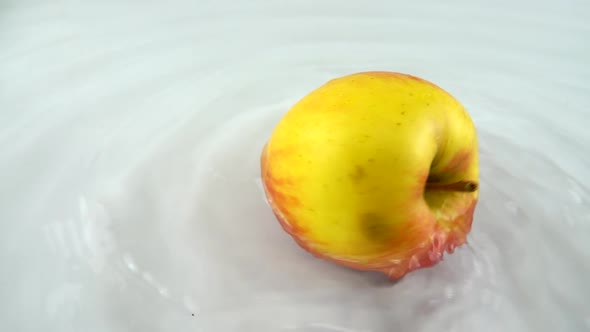 Rotating ripe apple in water on a white background. Slow motion.