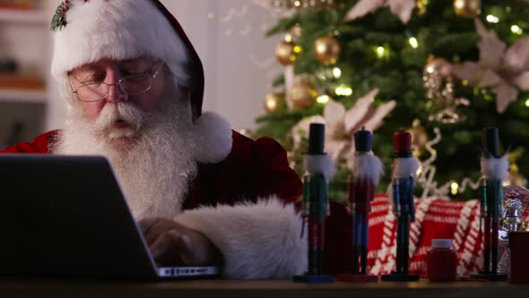 Santa Claus in workshop using laptop computer alt