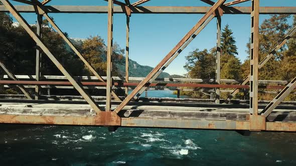 Drone rises from the water to the top of an old metal bridge to see the autumn landscape with the la