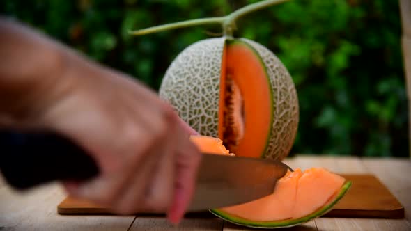 The man use knife split the orange melon on wood plate