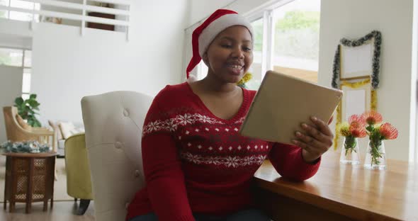 Happy african american plus size woman in santa hat, making video call using tablet at christmas