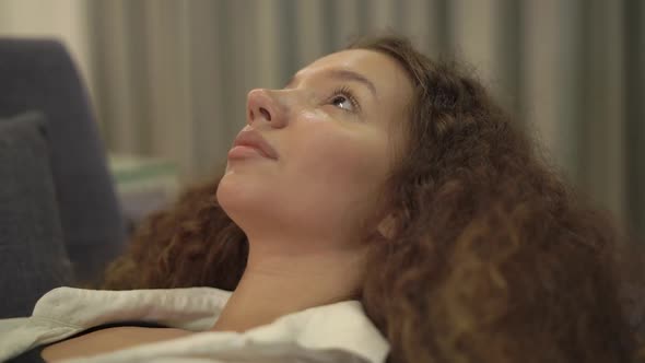 Thoughtful Young Woman with Curly Hair Stares at Ceiling