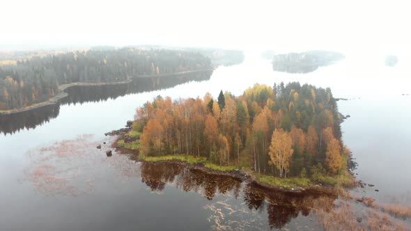 Aerial, tilt down, drone shot, flying over a island, full of autumn colors,, on a foggy, misty and c