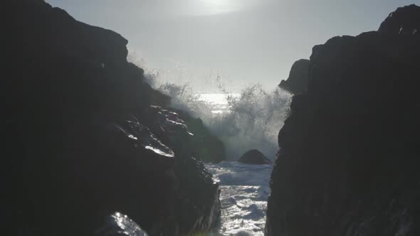 Slow motion low angle close up shot of an ocean wave smashing on rocks and flows towards camera