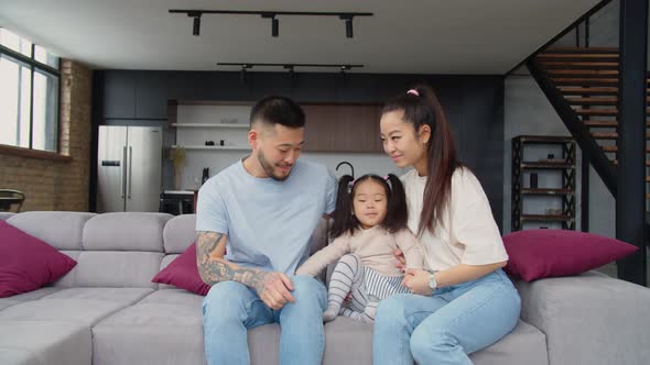 Happy Asian Parents and Baby Girl Waving Hand on Couch