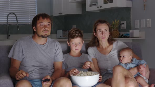 Happy Young European Family with Two Kids Gather on Couch to Watch TV at Home Smiling