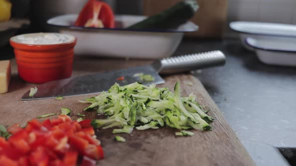 Diced zucchini/ courgette being dropped onto wooden chopping board. Home kitchen, diced red pepper i