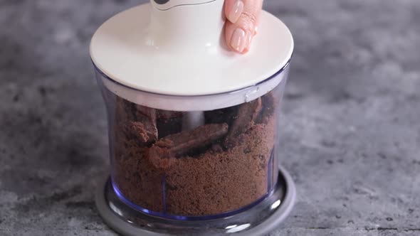 Female hands grinding chocolate cookies in a blender.