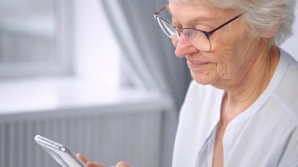 Delighted senior woman with short grey hair and glasses types on white smartphone