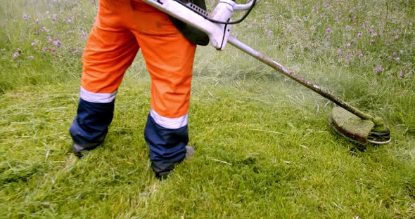 Worker in Orange Overalls Mows the Grass on the Lawn with a Gasoline Mower, Slow Motion Bsck View